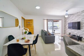 A modern living room with a sofa, dining table, and chairs. There is a television mounted on the wall and a door leading to a balcony. - Charming 3-bedroom apartment with Wi-Fi, AC in welcoming Santo Domingo Este. (Santo Domingo Este)