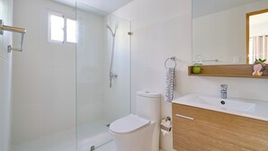 A bathroom with a glass-enclosed shower, a toilet, a sink, and a mirror with a wooden vanity.