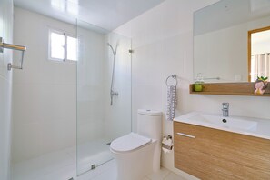A bathroom with a glass-enclosed shower, a toilet, a sink, and a mirror with a wooden vanity.