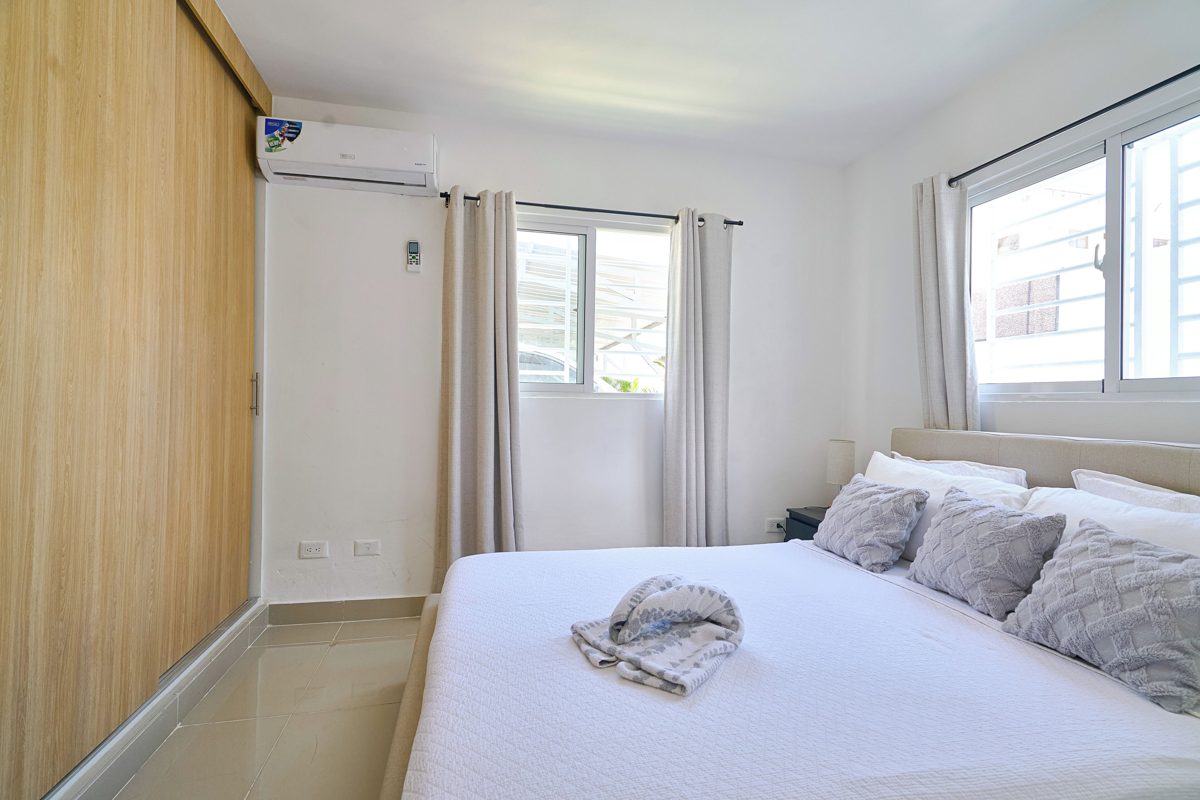 Una habitación de hotel con cama, cortinas, ventana y equipo de aire acondicionado.