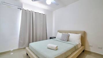A bedroom with a bed, a nightstand, a ceiling fan, and a window with curtains.