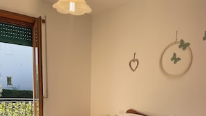 Un dormitorio con cama, mesita de noche, lámpara, ventana con vistas y puerta.