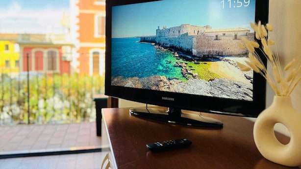 Un televisor Samsung sobre una mesa de madera mostrando una escena costera con la fecha y la hora.