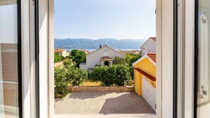 A view from inside a room looking out to a courtyard with a stone wall, a yellow building, and houses in the background. - 1 bedroom cozy apartment in Razanac (Razanac)