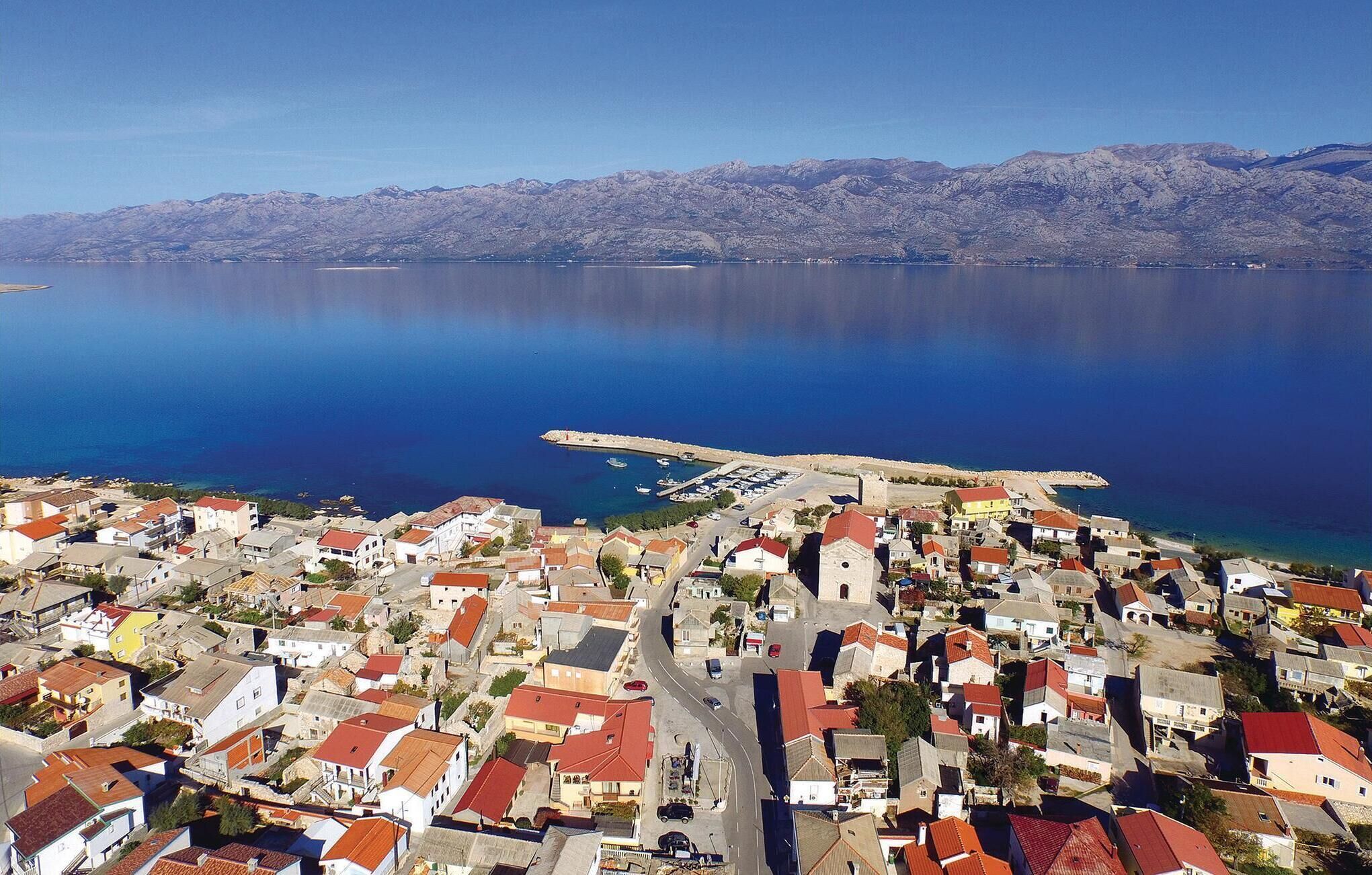 An aerial view of a coastal town with a marina, dense housing, and mountains in the background.