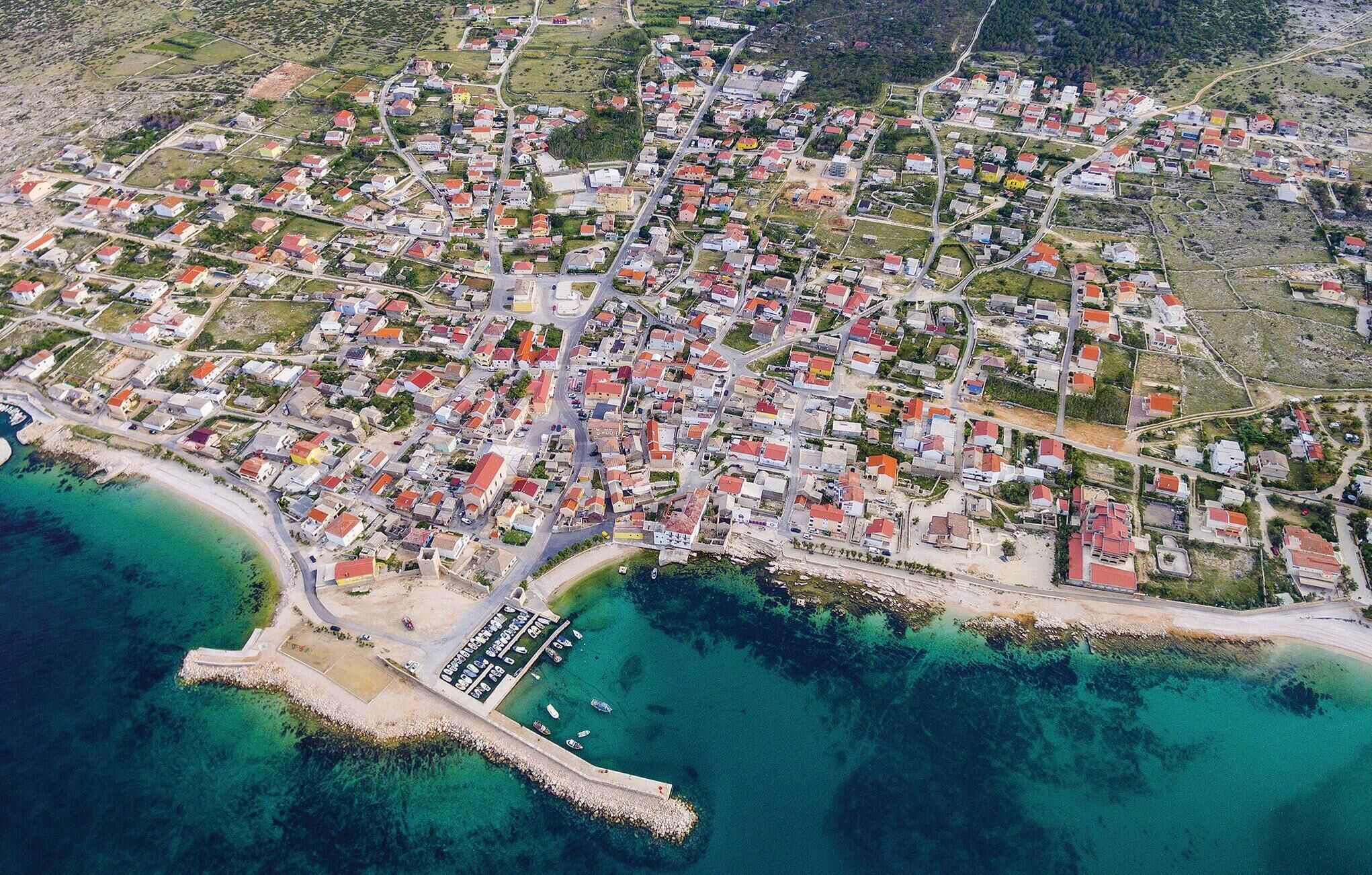 An aerial view of a coastal town with a marina, residential areas, and clear turquoise waters.