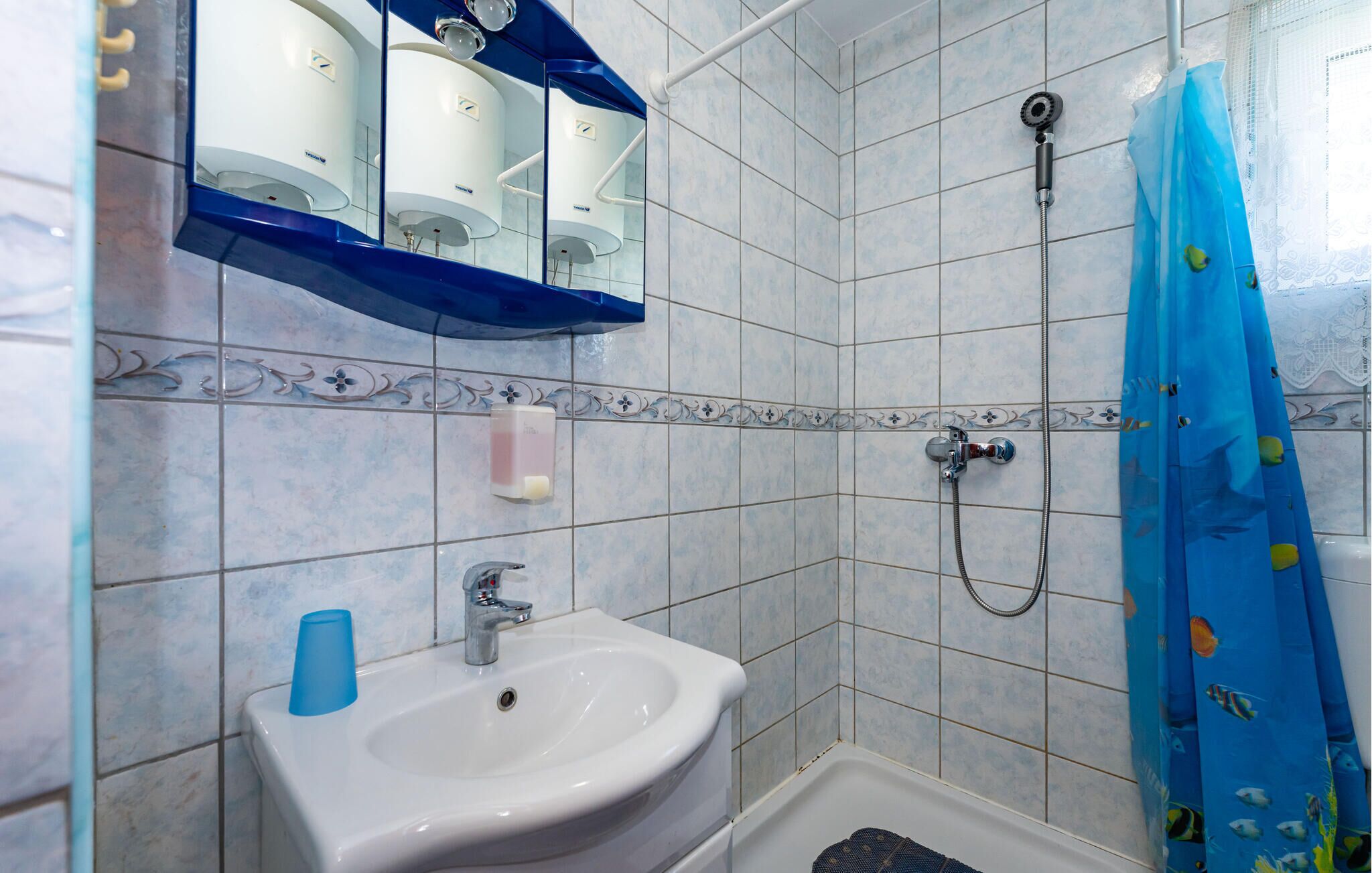 A bathroom with a sink, mirror, shower, and decorative tiles.