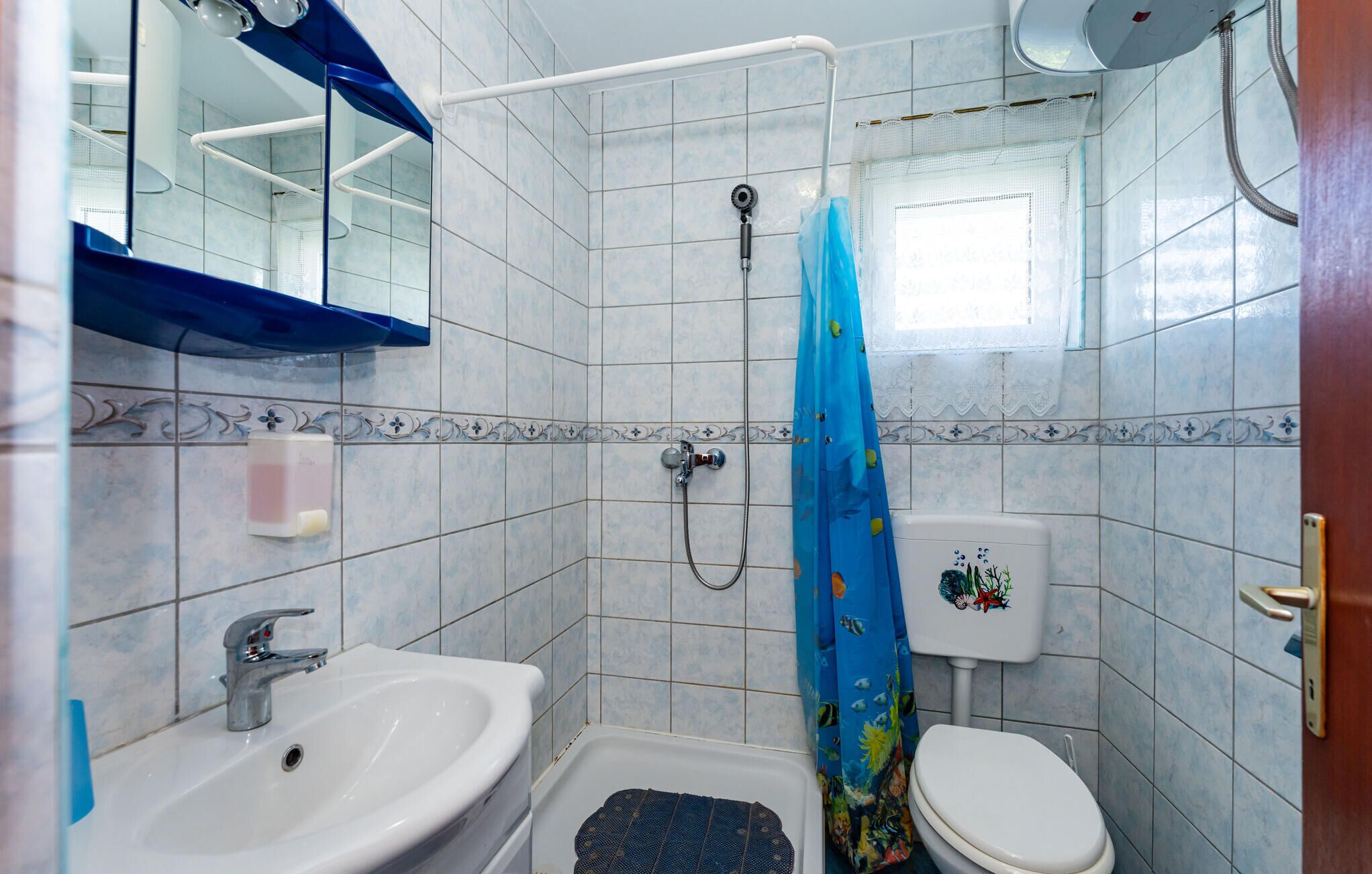Et badeværelse med bruser, toilet, vask og et vindue.