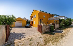 A yellow house with a garage, a car parked in front, and a stone wall with a gate. - 1 bedroom awesome apartment in Razanac (Razanac)