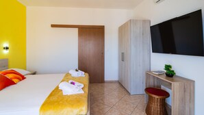 A hotel room with a bed, a TV, a wardrobe, and a small table with a plant.