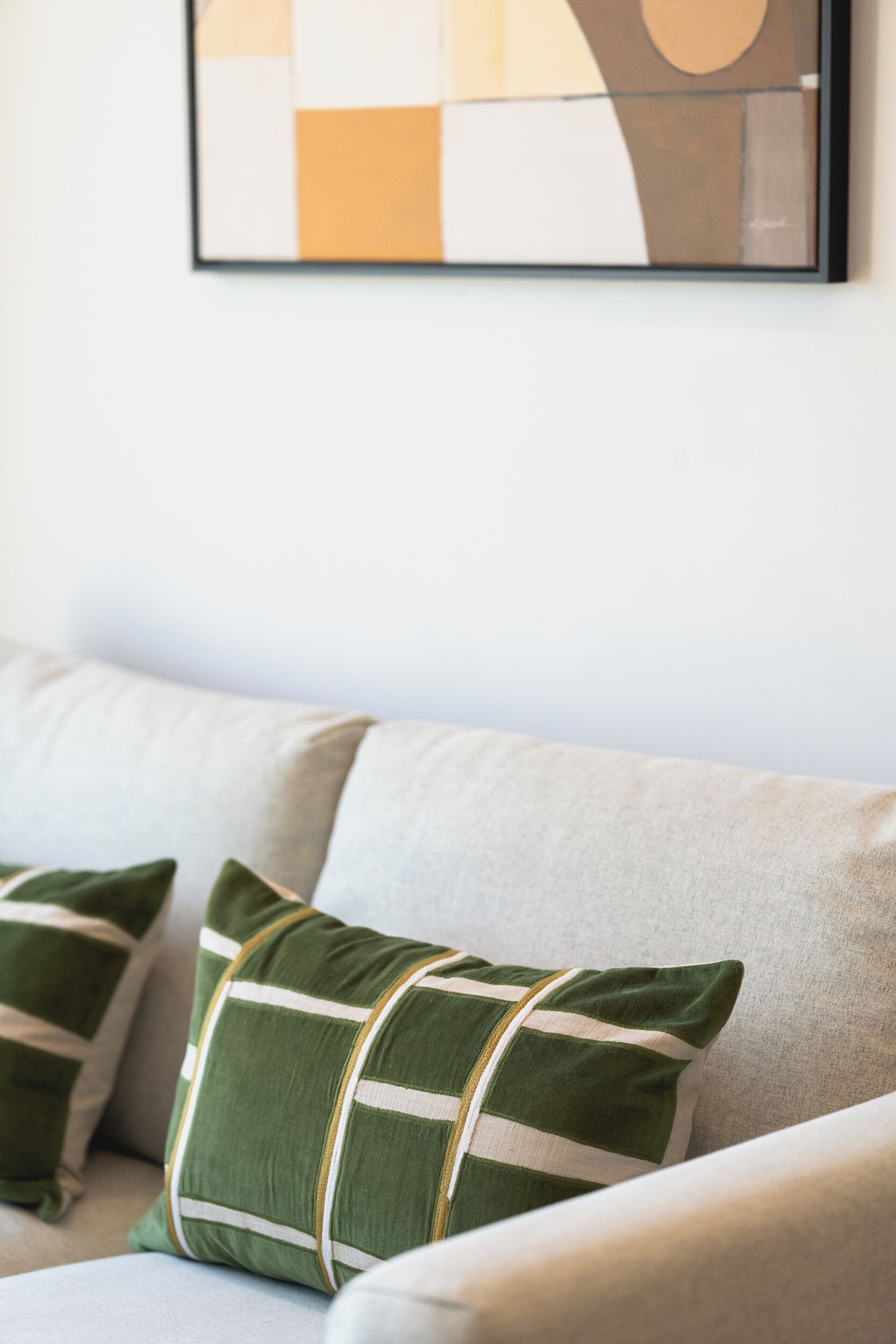 A sofa with two pillows, one striped and one plain, in a neutral-colored room.