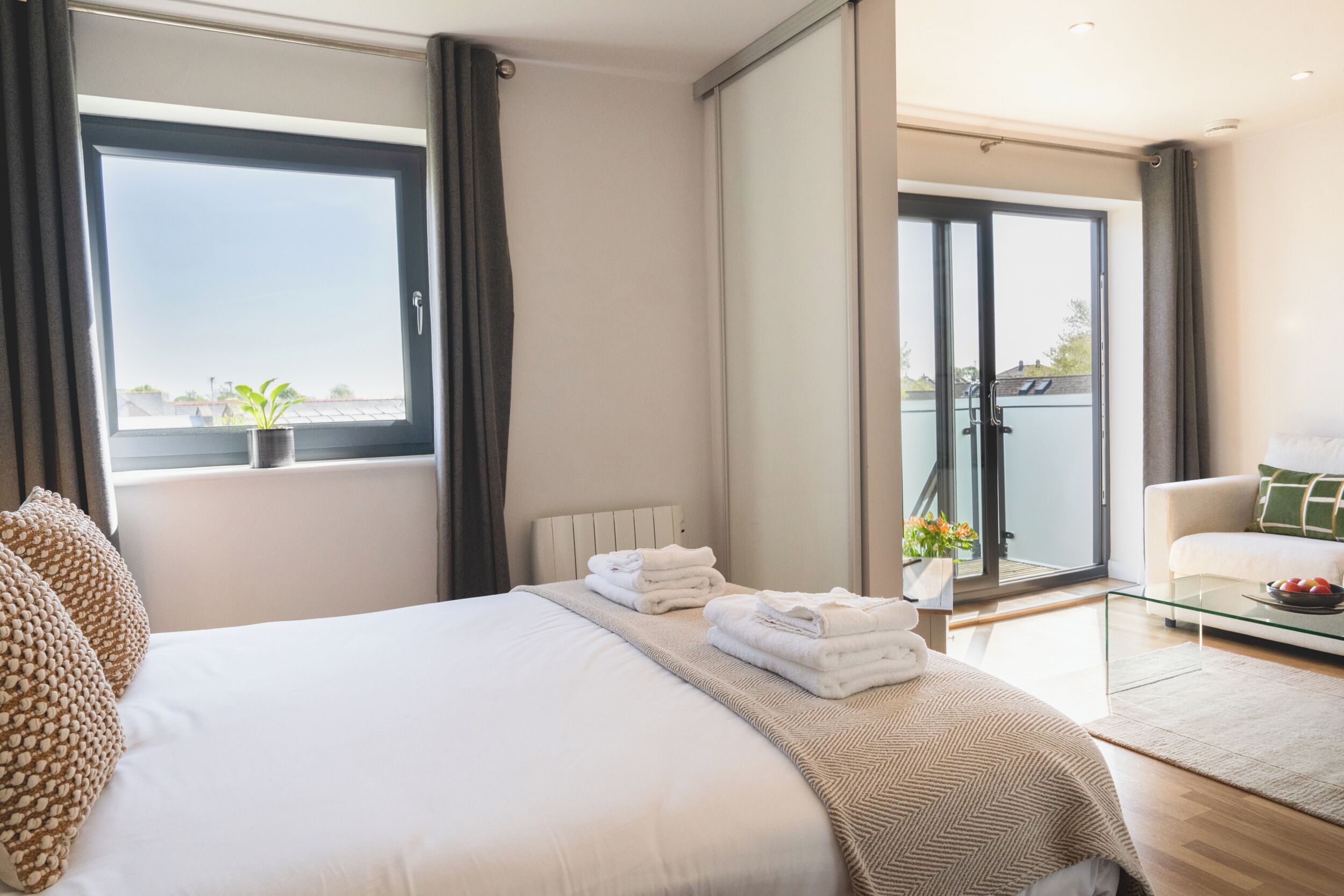 Une chambre d’hôtel moderne dotée d’un grand lit, d’une table basse en verre, d’un canapé et d’un balcon avec vue.