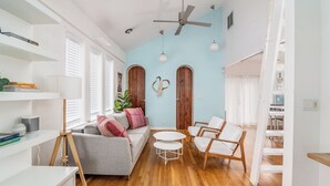 A modern living room with a grey sofa, white armchairs, a small white table, wooden flooring, and a ceiling fan.