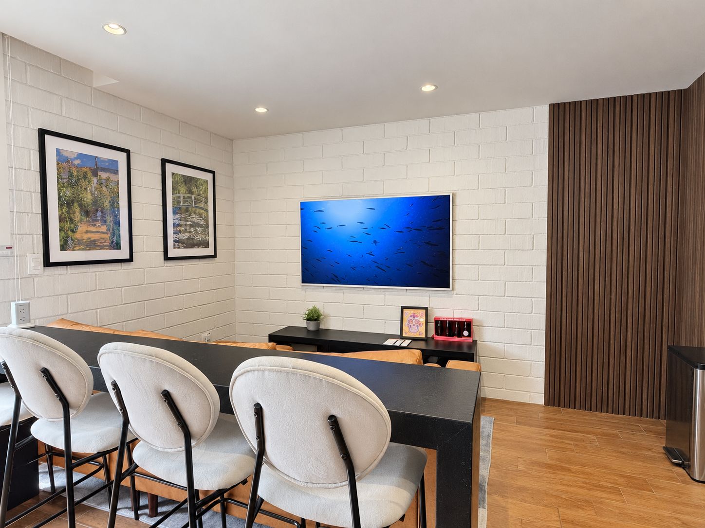 Un comedor moderno con una mesa negra, cuatro sillas, una pantalla de televisión grande y cuadros en la pared.