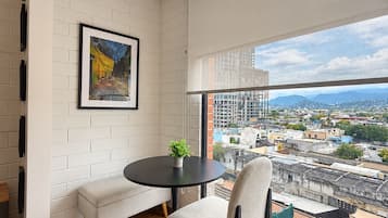 Ein modernes Zimmer mit großem Fenster, einem runden Tisch, einem Stuhl, einer Bank und einem gerahmten Gemälde an der Wand.