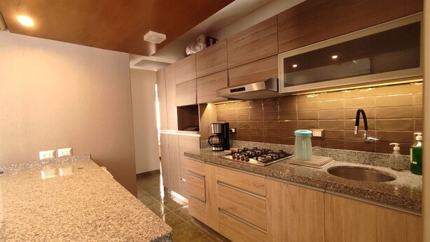 Una cocina moderna con encimeras de granito, armarios de madera, un lavamanos de acero inoxidable y una campana extractora empotrada.