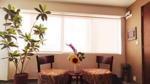 Una habitación con dos sillas estampadas, una planta en maceta y un florero con flores.