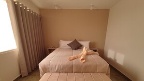 Una habitación de hotel con una cama grande, una mesita de noche, una lámpara y una ventana con cortinas.