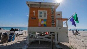 Et redderfyr med et flag, beliggende på en strand med klar himmel.