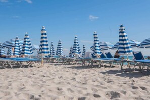 A beach with rows of blue and white striped umbrellas and lounge chairs.