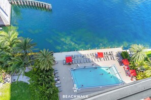 A rooftop pool area with lounge chairs and umbrellas, overlooking a clear blue body of water.