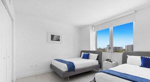 A modern bedroom with two beds, a city view, and a small bedside table with a plant.