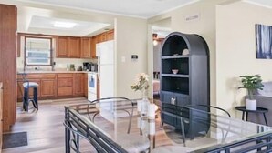 A modern kitchen with wooden cabinets, a glass dining table, and a built-in bookshelf.