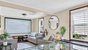 A modern living room with a glass coffee table, a sofa, a TV, and a large window with blinds.