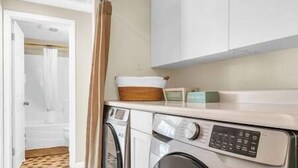 A laundry room with a washing machine and dryer, a wooden basket, and a small cabinet.