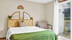 A bedroom with a bed, a headboard with framed quotes, a window with a view, and a ceiling fan.