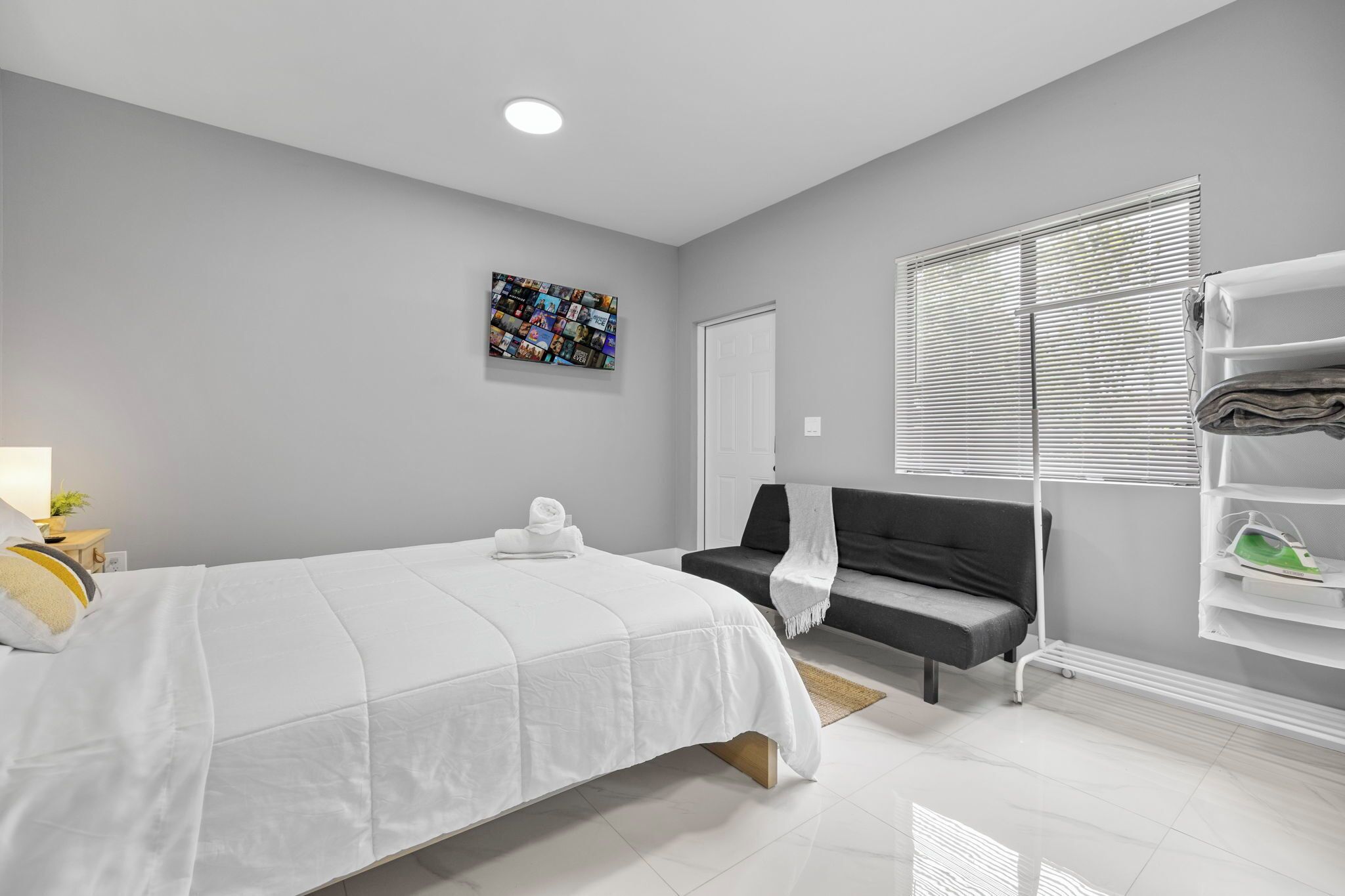 Un dormitorio moderno con cama, una banca, una obra de arte en la pared y un zapatero.