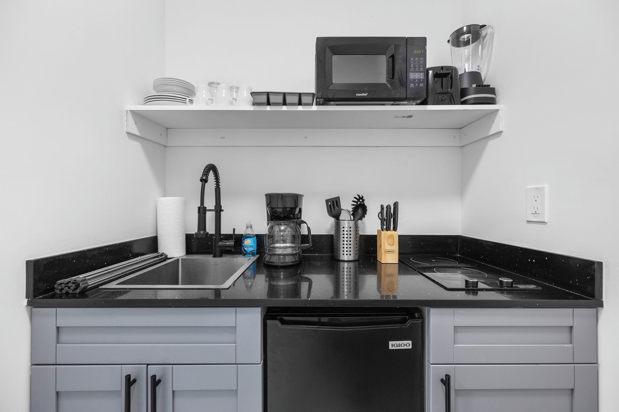 Cozinha com bancada preta, micro-ondas, cafeteira e máquina de lavar louça.