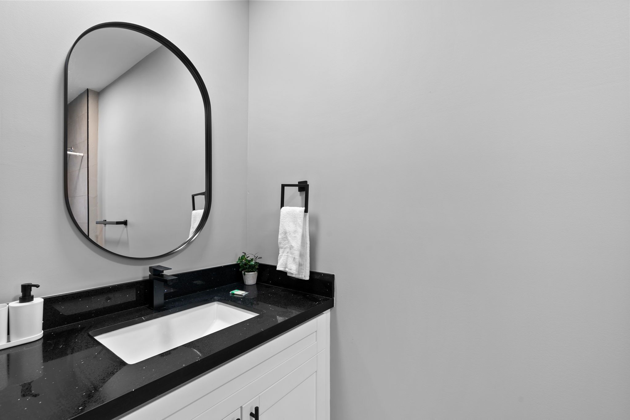 A modern bathroom with a black countertop, white sink, and a large oval mirror.