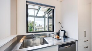A modern kitchen with a stainless steel sink, a window with a view of houses, a coffee machine, and a dishwasher.