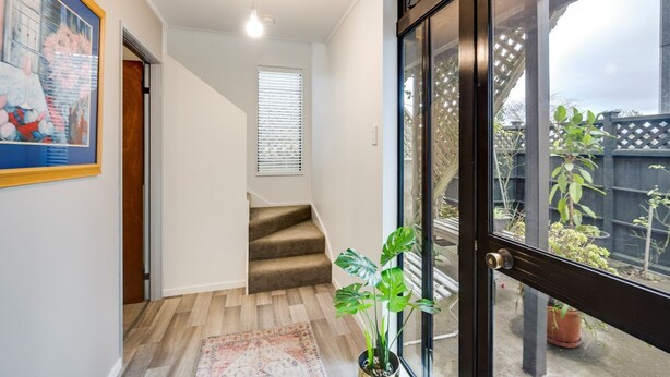 A hallway with a carpeted staircase, a potted plant, and a large window with a view of the outside.