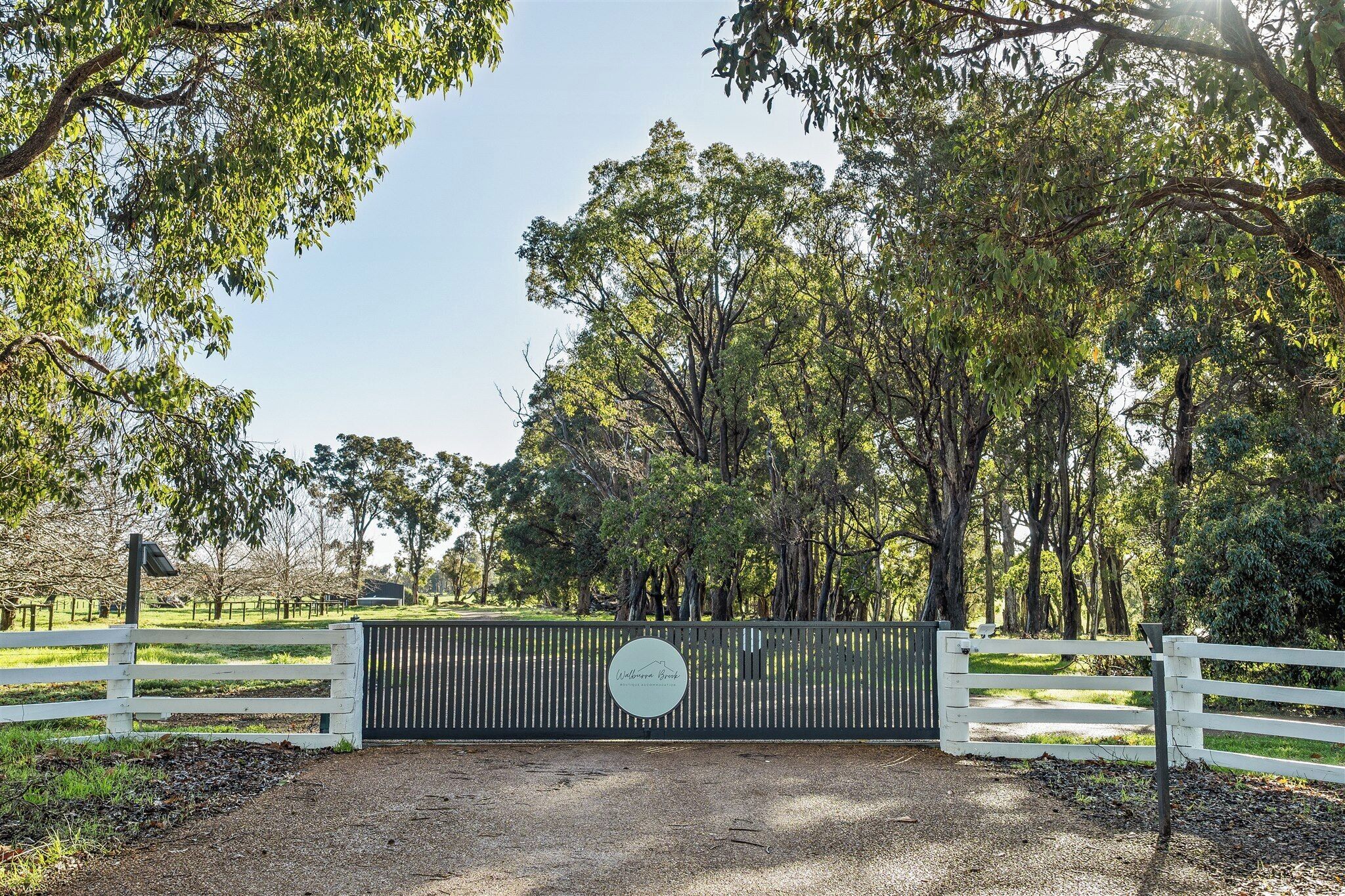 A gated entrance with a sign, surrounded by trees and a gravel path.