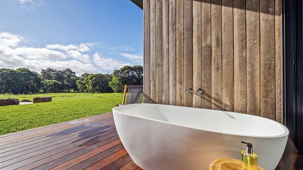 A modern outdoor bathtub on a wooden deck with a view of a grassy field and trees. - Chalet Coast | Walburra Brook Off-grid Luxury stay (Metricup)