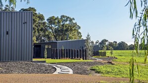 A modern building with a metal exterior, surrounded by a landscaped garden and trees. - Chalet Coast | Walburra Brook Off-grid Luxury stay (Metricup)