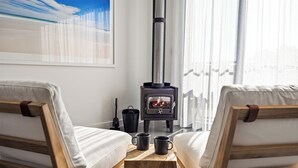 A cozy room with two wooden chairs, a small table with two mugs, and a wood-burning stove. - Chalet Coast | Walburra Brook Off-grid Luxury stay (Metricup)