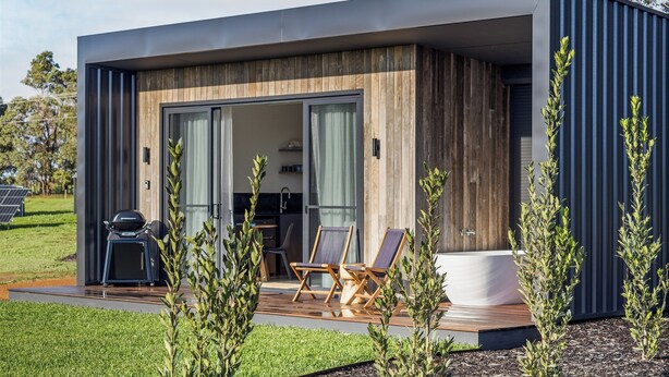 Una casa moderna con fachada de madera, una terraza con sillas y una barbacoa, y una bañera blanca grande.