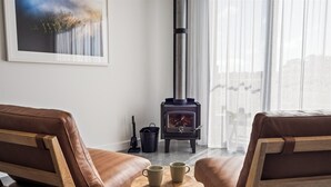 Un salón acogedor con dos sofás de cuero marrón, una mesita de madera con dos tazas y un estufa de leña de color negro.