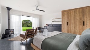 Un dormitorio moderno con una cama grande, un armario de madera, una chimenea empotrada y vistas a un paisaje verde.