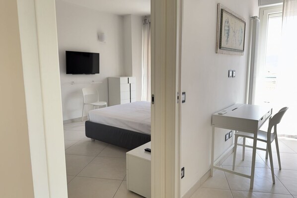 A modern hotel room with a bed, a desk, a chair, a television, and a painting on the wall. - Exclusive Penthouse, Sea View, 100m from the beach (Alassio)