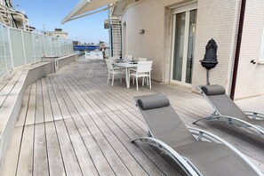 Une terrasse en bois avec une table et des chaises, un fauteuil de relaxation et une fontaine à eau fixée au mur.