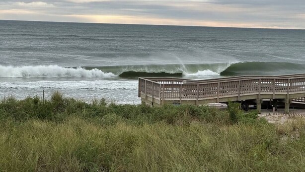 Una pasarela de madera que conduce a una playa con olas rompiendo en la orilla.