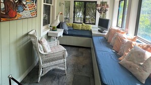 Una habitación acogedora con un banco empotrado, una silla de mimbre, una mesa con lámpara y un cuadro en la pared.