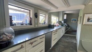 Una cocina amplia con una encimera larga, armarios blancos y piso de baldosas de piedra.