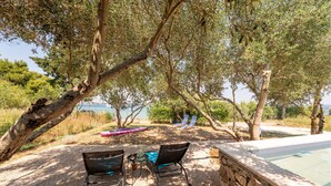 An outdoor seating area with two chairs and a table, overlooking a pool and a body of water.