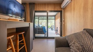 A modern living room with a sofa, a TV, a wooden table, and a sliding glass door leading to an outdoor area.