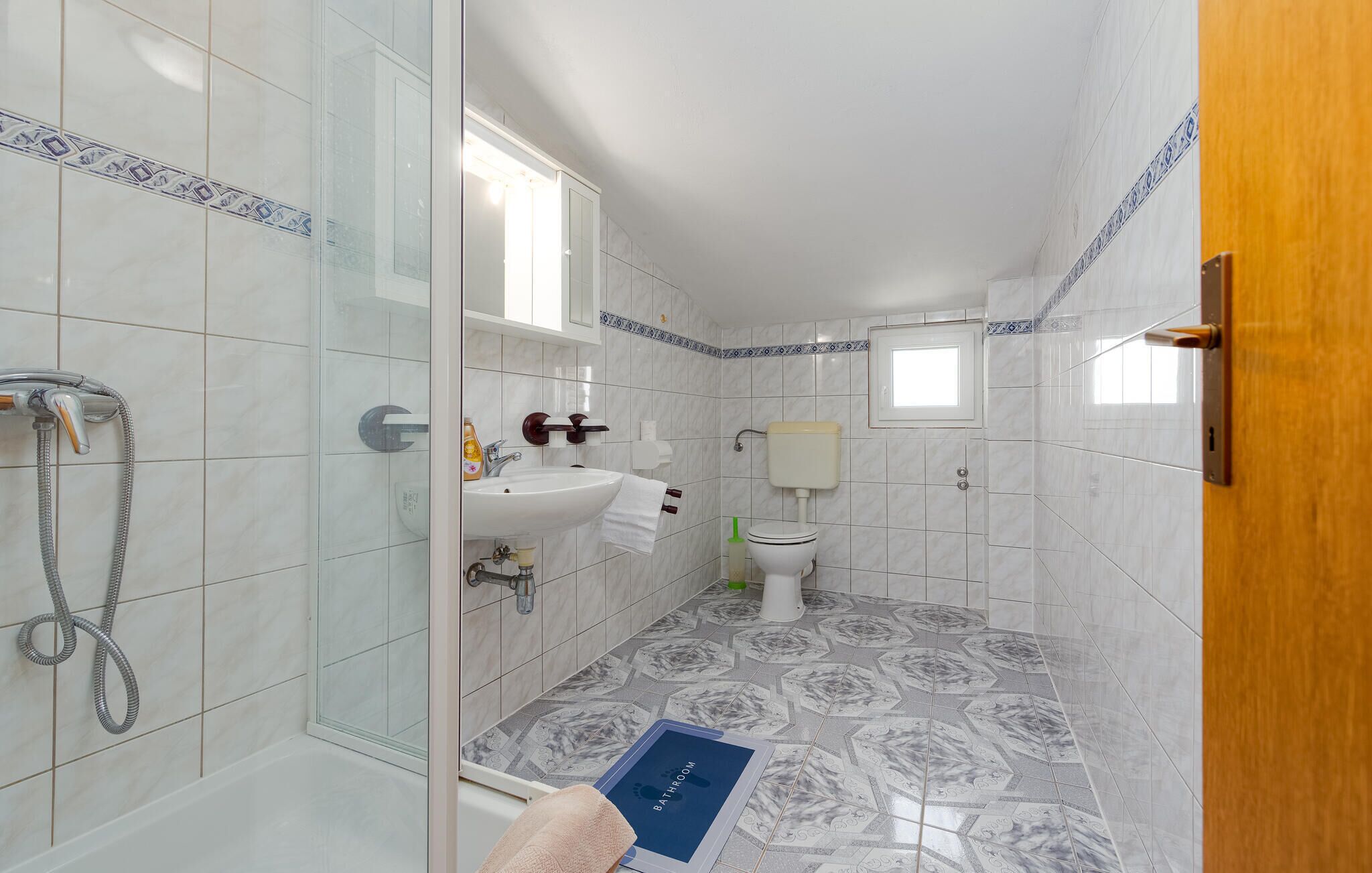 A bathroom with a glass shower enclosure, a sink, a toilet, and a small window.